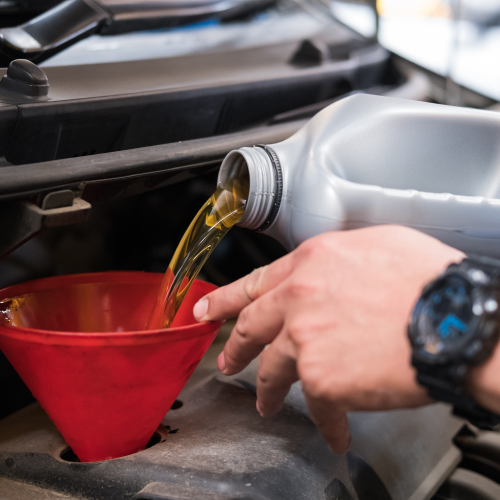 Una mano vierte aceite de motor a través de un embudo rojo en el motor de un automóvil, destacando el proceso esencial de cambio de aceite para el mantenimiento y buen funcionamiento del vehículo.