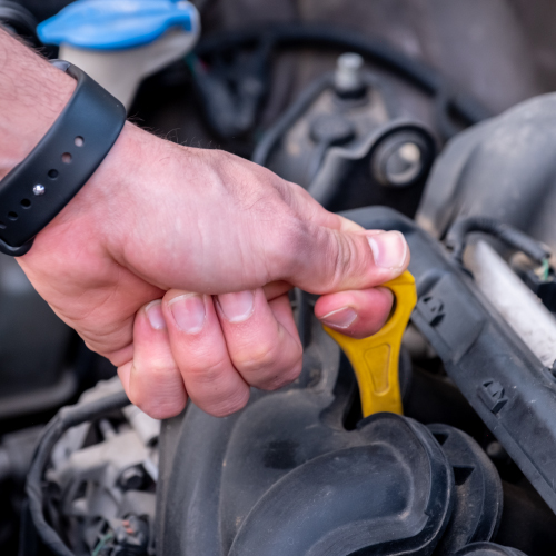 Una mano sostiene una varilla de medición de aceite de motor amarilla en el compartimiento del motor de un automóvil. La imagen ilustra la tarea esencial de verificar el nivel de aceite del motor para asegurar su correcto funcionamiento y mantener el vehículo en óptimas condiciones.