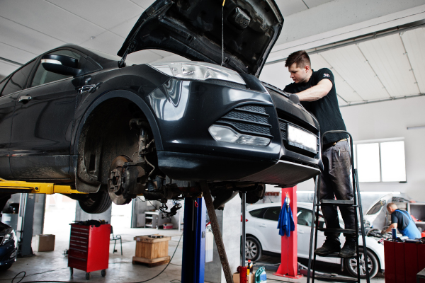 Un mecánico trabajando en el motor de un automóvil elevado en un taller.