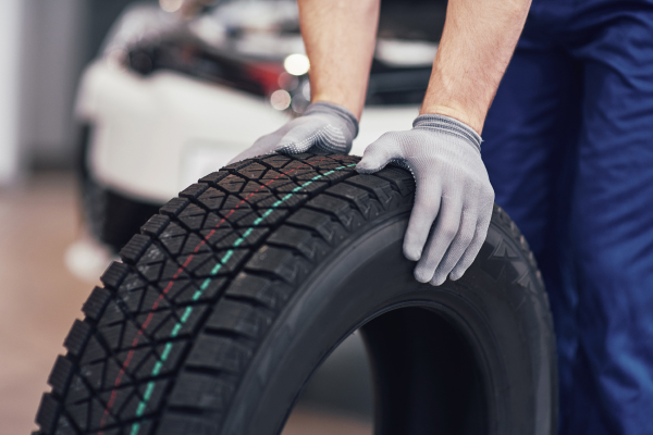 Una persona con guantes manipulando una llanta nueva en un taller mecánico, con un automóvil desenfocado en el fondo.