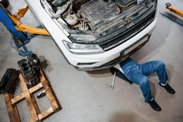 Un mecánico revisando el motor de un automóvil en un taller, con herramientas y piezas a su alrededor.