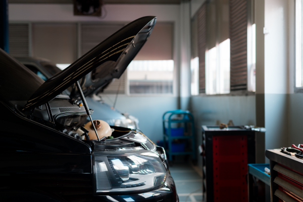 Un coche de color negro con el capó abierto en un taller mecánico.