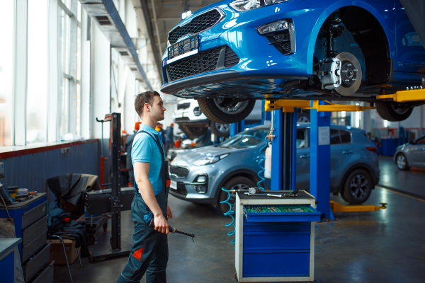 Un mecánico trabaja en un coche azul elevado en un taller de automóviles.