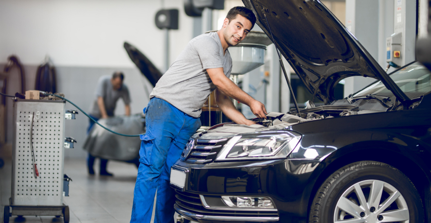 Un mecánico de taller está revisando el motor de un coche azul.