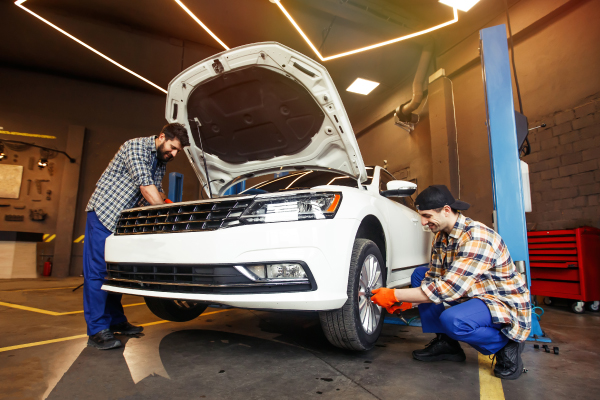 Dos mecánicos trabajando en un coche blanco en un taller de reparación.