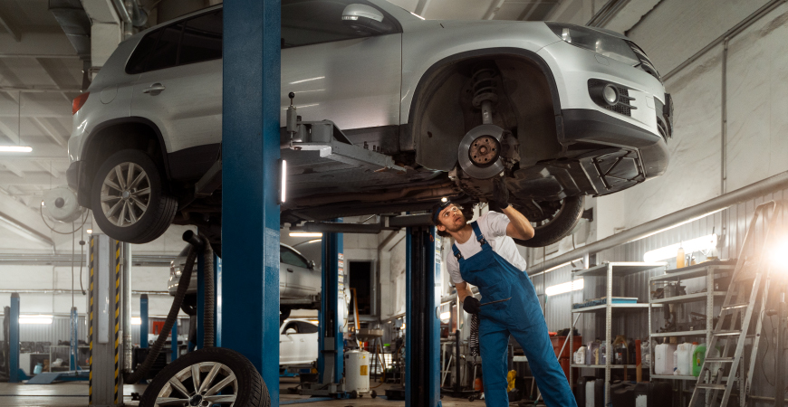 Un mecánico trabajando en un SUV plateado en un taller de reparación de automóviles.