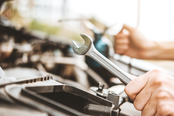 Un mecánico usando una llave inglesa para trabajar en el motor de un automóvil. Esta actividad de mantenimiento y reparación es esencial para el buen funcionamiento de los vehículos.